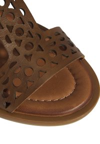 Braune Sandale mit einem ausgeschnittenen Muster, das Kreise und Dreiecke zeigt. Hergestellt aus weichem Leder mit einer braunen, strukturierten Innensohle und gestickten Akzenten.