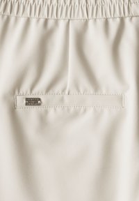 Beige shorts met elastische tailleband, een gladde textuur en een klein metalen merkje genaaid op de achterzak.