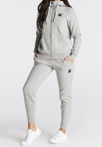 Grijze hoodie met rits en bijpassende joggingbroek van zacht materiaal, met geribbelde manchetten en zakken. Kleine zwarte logo op de borst.