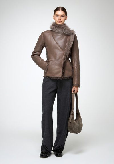 Giacca di pelle marrone con colletto in pelliccia sintetica, design asimmetrico e tasche laterali. Abbinata a pantaloni grigi a gamba larga e una borsa in suede marrone.