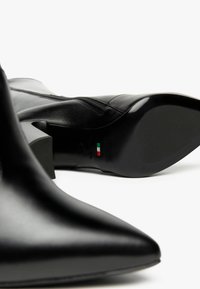 Stivaletti neri in pelle con punta affilata, superficie liscia e tacco spesso. Dettaglio con zip laterale e branding italiano sulla suola.