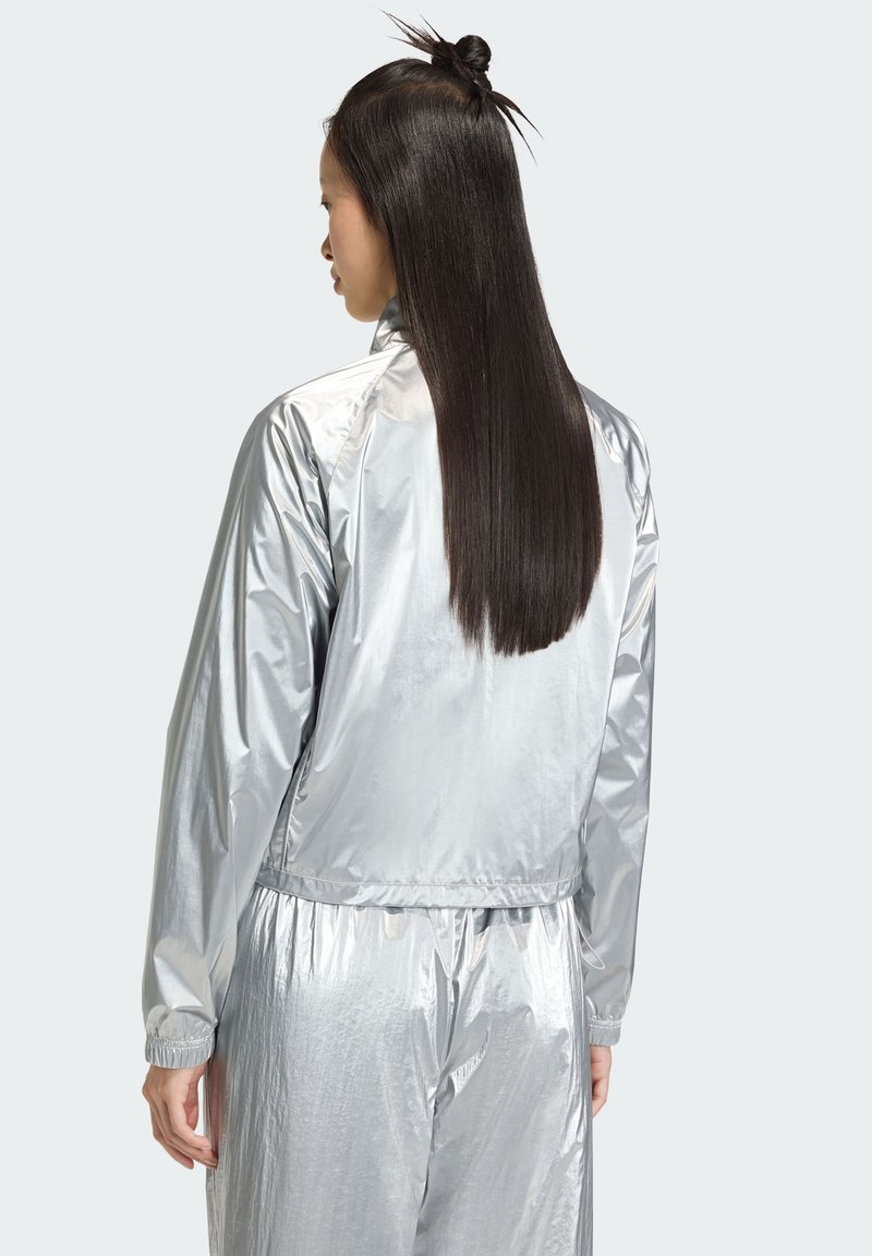 Veste bomber argentée avec une texture brillante et lisse. Dotée de poignets et d'une taille élastiques, conçue pour une coupe décontractée.