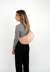 Borsa a tracolla in morbido rosa cipria realizzata in tessuto liscio, con un design curvo e dettagli con logo. Indossata sulla schiena. Include una tracolla regolabile.