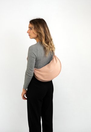 Borsa a tracolla in morbido rosa cipria realizzata in tessuto liscio, con un design curvo e dettagli con logo. Indossata sulla schiena. Include una tracolla regolabile.