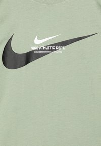 Vaaleanvihreä Nike-t-paita, jossa on suuri musta swoosh ja valkoiset tekstit "NIKE ATHLETIC DEPT. ENGINEERED FOR ALL ATHLETES."