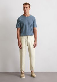 Blaues Rundhals-T-Shirt, lockere Passform; hellfarbene Leinenhosen, am Knöchel umgeschlagen; beiges Schnürschuh; glatte Textur.