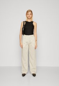 Zwart mouwloos topje met een gebogen halslijn, crème wijde broek met verticale strepen en zwarte puntige flats. Minimalistische stijl.