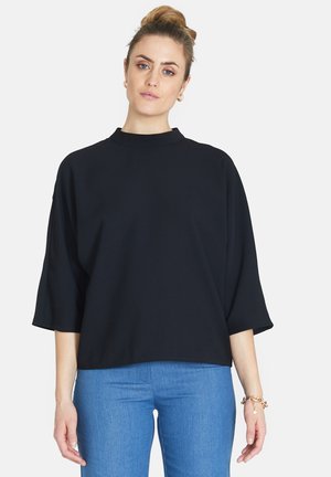 Czarna, luźna bluzka z wysokim kołnierzem i szerokimi rękawami. Miękki materiał, minimalistyczny design. W połączeniu z jasnoniebieskimi, dopasowanymi dżinsami.
