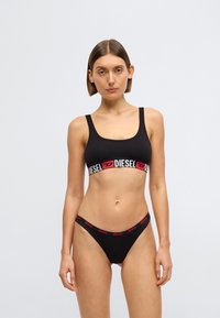 Must spordirinnahoidja ja sobivad bikiinipõhjad, mille vöökohal on lai punane ja valge elastne riba koos "DIESEL" logoga. Sile tekstuur.