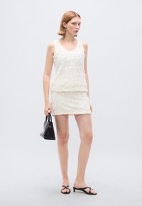 Λευκό αμάνικο φόρεμα με υφή ανθών και στενή μίνι φούστα. Συνδυασμένο με μαύρα αξεσουάρ, που περιλαμβάνουν μια μικρή τσάντα και σανδάλια.