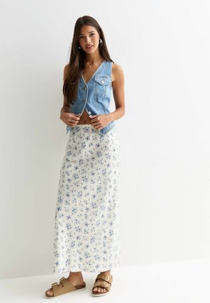Jeansväst med knappar och sidofickor, i kombination med en blommig maxikjol i vitt och blått. Bruna sandaler med spännen fulländar looken.