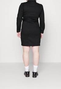 Robe noire à manches longues, avec une taille ceinturée et un bas légèrement évasé. Le matériau est lisse ; présente des détails de manches bouffantes.