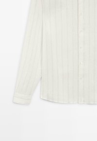 Long-sleeve white button-up shirt with subtle vertical stripes and cuffed sleeves, shown from mid-torso to wrist.