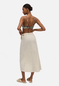 Top corto de halter verde con estampado y tirantes finos, combinado con una falda maxi de lino beige que presenta un detalle de cintura atada y una textura suave.