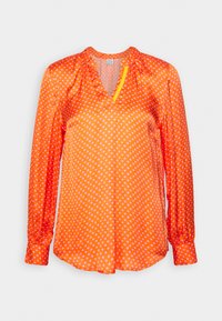 Blouse à manches longues orange vif avec des pois blancs, un col rond froncé et un petit accent jaune près de l'ouverture en V.
