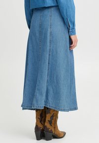 Denim maxikjol i ljusblått, med sömdetaljer och en utsvängd form. Aningen med bruna cowboystövlar och en blå blus.