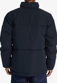 Mörkblå puffjacka med hög krage, med horisontella sömmar och avslappnad passform. Texturen ser slät ut, utformad för värme.