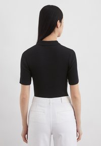 Zwarte geribde poloshirt met korte mouwen, voorzien van een klassieke kraag. Draag het met witte broeken met hoge taille, wat zorgt voor een aangesloten silhouette.