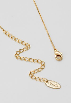 Złoty naszyjnik z łańcucha z zapięciem typu lobster i owalną zawieszką z wygrawerowanym słowem "Orelia" na białym tle.