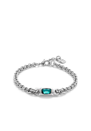 Bracelet en chaîne argentée avec une gemme en turquoise taillée en émeraude, des maillons entrelacés et un fermoir lobster agrémenté d'un petit charme.