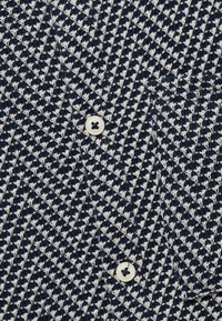 Camicia a righe blu navy e bianca con un motivo a spina di pesce, tessuto testurizzato e due bottoni tondi color crema sul davanti.