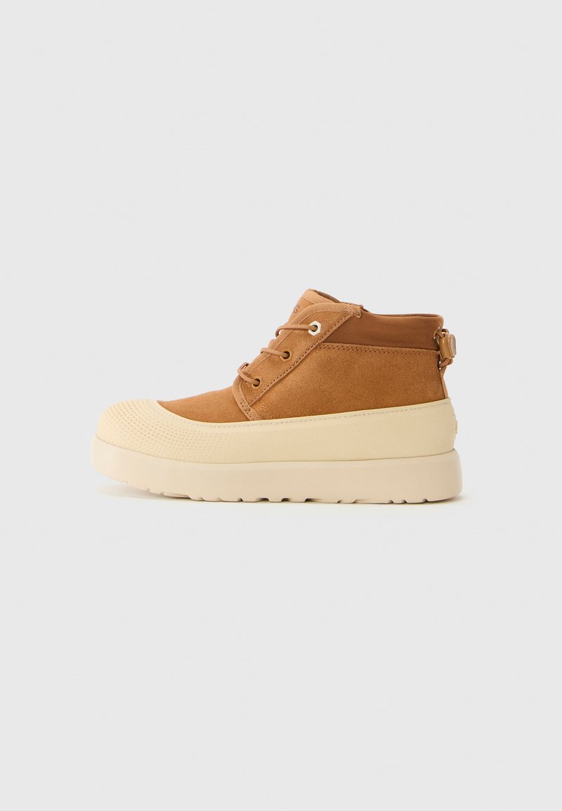 Botte de cheville en daim brun à lacets avec une épaisse semelle en caoutchouc crème et un bout texturé, présentée en profil latéral sur fond uni.