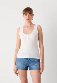 Hvit ribbet singlet med en dyp utringning og tre-knappers placket, sammen med blå denimshorts med frynset kant.