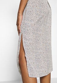 Kukkakuvioinen hame, jossa valkoinen tausta, pieniä monivärisiä pisteitä, korkea halkio sivussa, pehmeä kangas ja puolipitkä muoto.