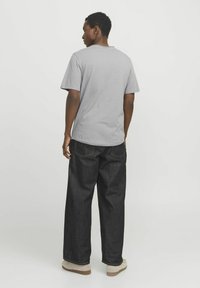 Graues T-Shirt mit kurzem Arm und Rundhalsausschnitt, kombiniert mit lockeren, dunklen Jeans und beigen Schuhen. Einfaches, minimales Design.