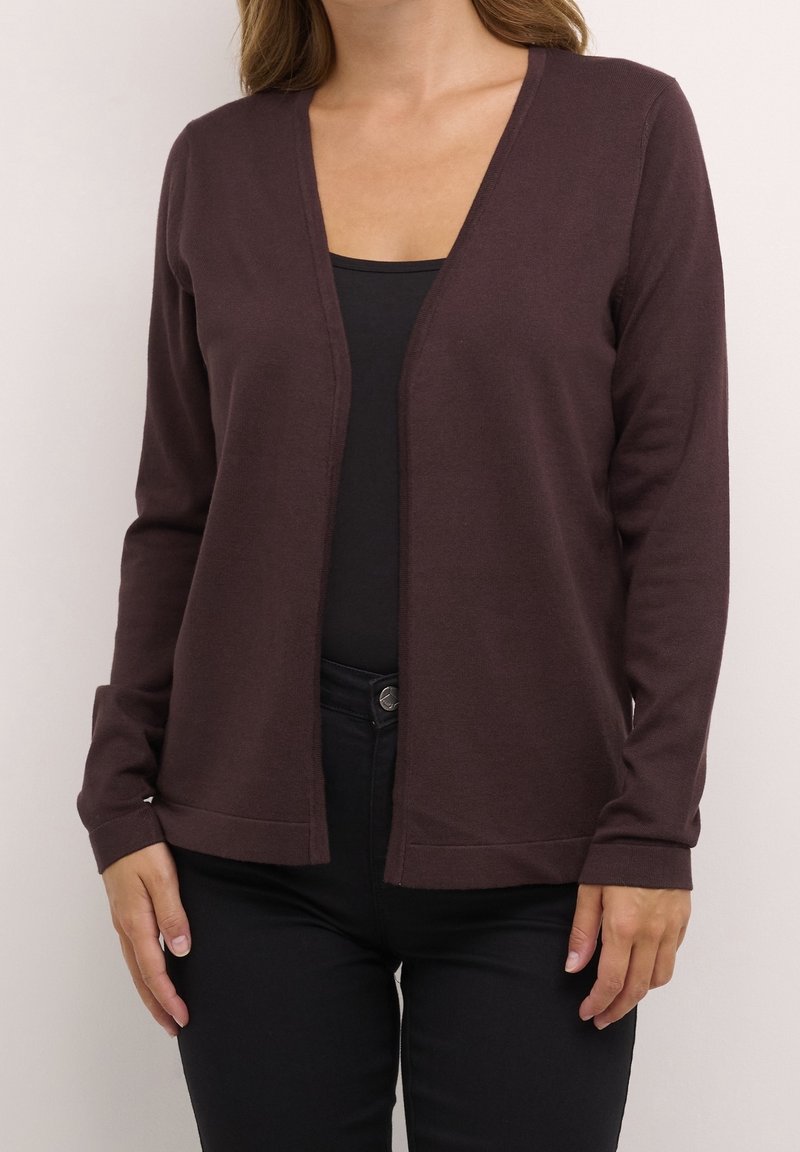 Cardigan marron à manches longues en tissu doux avec un décolleté en V profond et des poignets ajustés, porté sur un haut noir et associé à un pantalon noir.