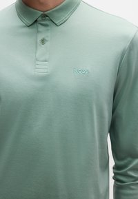 Hosszú ujjú póló puha menta zöld anyagból. Klasszikus gallérral, háromgombos elülső Résszel és a "BOSS" logóval hímzett, ugyanolyan színben.