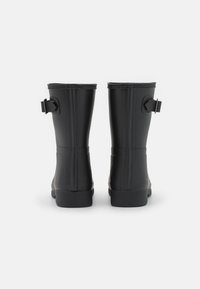 Botas de lluvia de goma negras con acabado texturizado, forma recta y correas ajustables en los tobillos. Suela sólida y sin patrones.