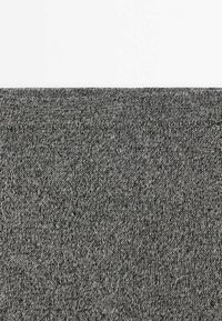 Gros plan d’un tissu tricoté gris foncé texturé avec une couture horizontale visible près du bord supérieur.
