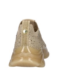 Chaussure de sport en tricot beige avec une surface texturée, des accents en strass et une semelle en caoutchouc brillante. Dotée d'un onglet de talon renforcé pour un enfilage facile.
