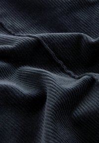 Texturerad mörkblåt tyg med framträdande ribbat mönster, som visar en mjuk, plyschyta och mjuka veck.