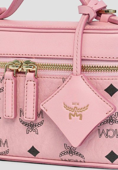 Gros plan sur un sac à main en cuir rose avec une fermeture éclair dorée, doubles curseurs de fermeture éclair, étiquette du logo MCM et motifs imprimés noirs.