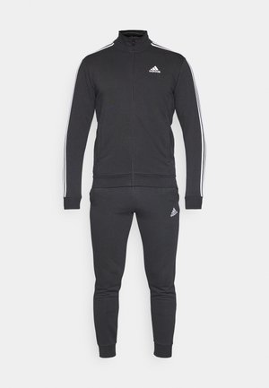 Black tracksuit made of a durable fabric, featuring a zip-up jacket with white stripes and matching tapered pants with a logo on the chest and thigh.