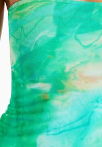 Haut sans manches vert en tissu léger et extensible, présentant un motif tie-dye dans des nuances de turquoise et de pêche clair.