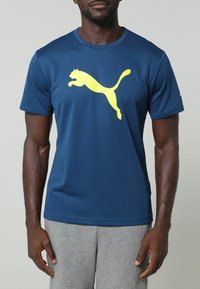 Marineblå kortärmad tränings-T-shirt i fukttransporterande tyg. Har en stor gul Puma-logotyp på framsidan och klassisk rund halsringning.