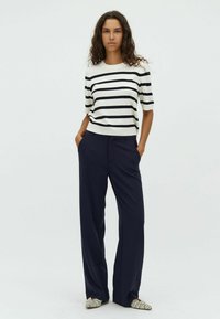 Striped knit top in cream and navy, paired with navy wide-leg pants. Textured fabric, relaxed fit, and animal print shoes.