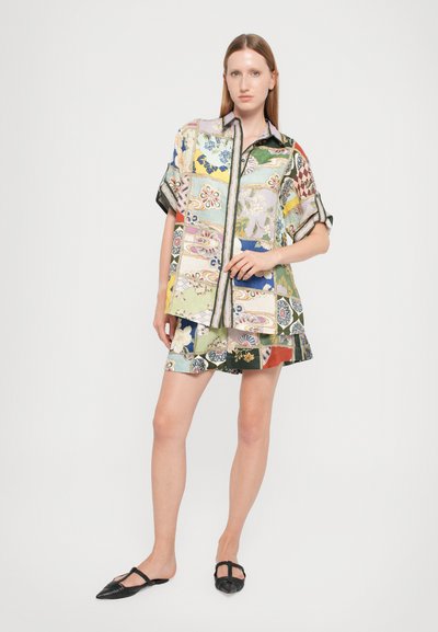 Multicolored oversized shirt with patchwork design, featuring floral and geometric patterns, paired with matching shorts and black slip-on shoes.