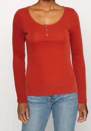Long-sleeve ribbed top in burnt orange with a scoop neckline and three-button detail at the chest. Soft texture and fitted design.