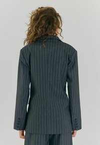 Mørkegrå blazer med nålestriber, skræddersyet pasform, klapkrave og tre-knaps manchetter. Glat stof med et struktureret design og rygslids.