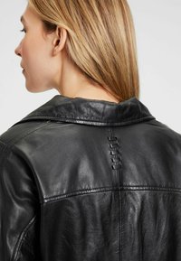 Schwarze Lederjacke mit glatter Textur, breitem Kragen und dekorativer Naht entlang der Rückennaht. Verfügt über ein schlankes, modernes Design.