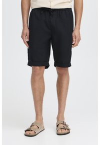 Black shorts with a relaxed fit, elastic waistband and drawstring, rolled cuffs, made from lightweight fabric, paired with beige sandals.