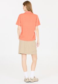 Korte mouwen, koraalkleurig polo-shirt gecombineerd met een beige skort, met een zijzak en een relaxte pasvorm. Gdragen met witte enkelsokken en lichte schoenen.