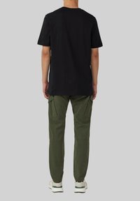 Zwarte katoenen t-shirt, korte mouwen, relaxte pasvorm, gecombineerd met groene cargobroek met zijzakken en taps toelopende pijpen, gedragen met witte sneakers.