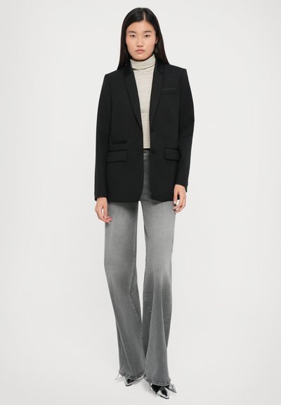 Black blazer with a notched lapel, two front pockets, worn over a striped turtleneck. Paired with flared gray jeans and pointed-toe heels.