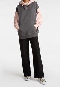 Šedá a růžová mikina s kapucí a barevnými bloky, s přední kapsou a šňůrkami na stažení, v kombinaci s černými širokými kalhotami a kostkovanými nazouvacími botami.