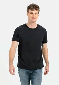 Sort bomulds t-shirt med rund hals, korte ærmer og et diskret logo. Kombineret med blå denim jeans. Blød tekstur, tætsiddende design.